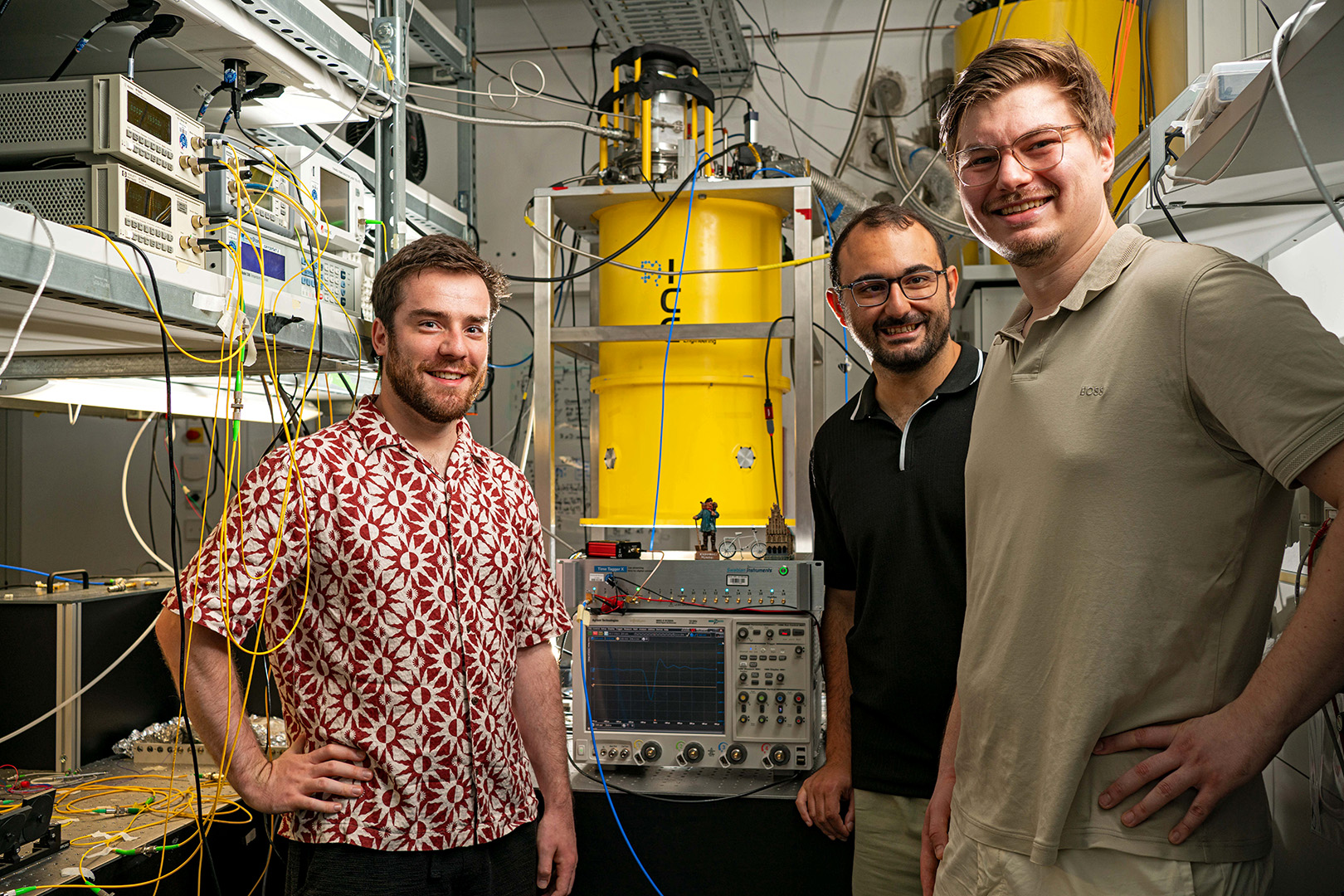 Three researchers from Münster University, standing beside their Light Detection and Ranging time of flight measurement setup, which includes optical components and equipment on an optical table. Credit: Jonas Klempel