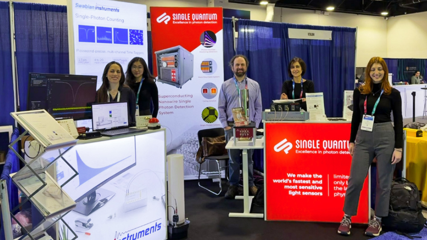 Swabian Instruments and Single Quantum team members at their joint exhibition booth at APS Global Physics Summit 2026 in Denver. From left to right: Mireia Perera-González and Ginger (Tingting) Geng from Swabian Instruments, and Katyayani Seal from Single Quantum. The Swabian Instruments banner highlights "Single-Photon Counting" applications, and the Single Quantum backdrop reads "Excellence in photon detection." Instrumentation for a standard lifetime demonstration and a laptop displaying a histogram curve being built on the graphical user interface are visible on the booth counter.