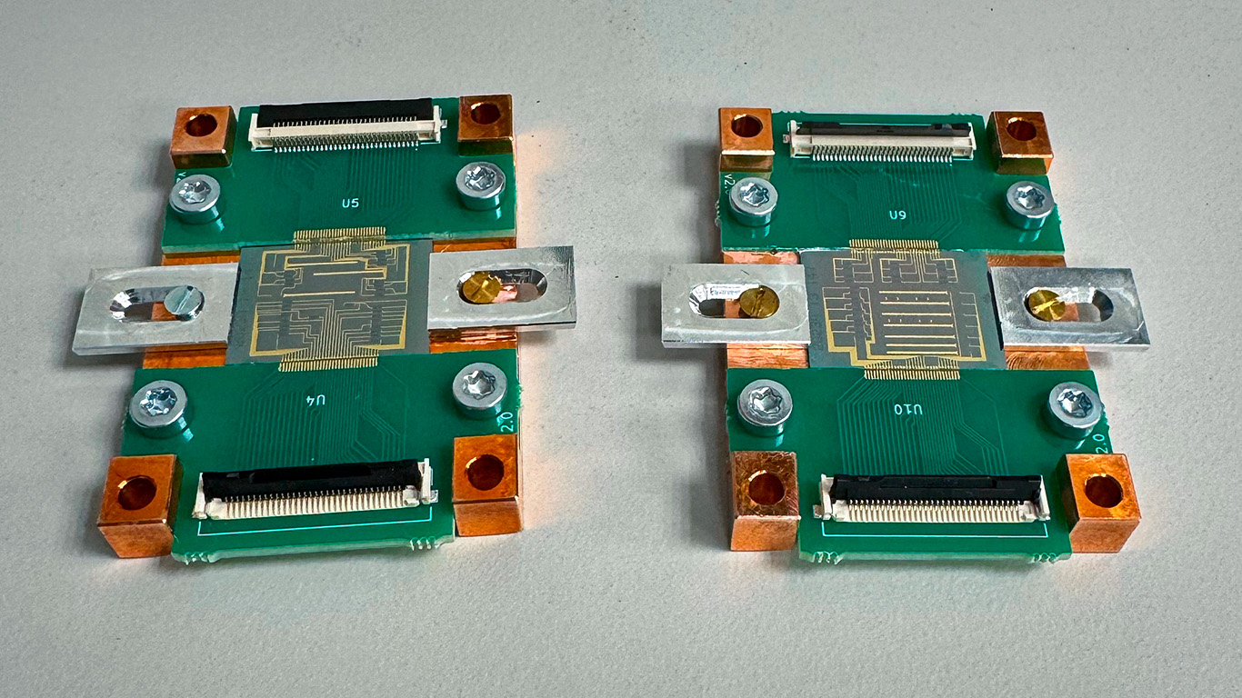 Two green thin-film lithium niobate photonic integrated circuits mounted on copper-cornered Printed Circuit Boards with silver clamps and Flexible Printed Circuit connectors, used for generating, distributing, and measuring time-bin entangled photon pairs in quantum photonics research. (Image credit: Dr. Robert Chapman, ETH Zürich)